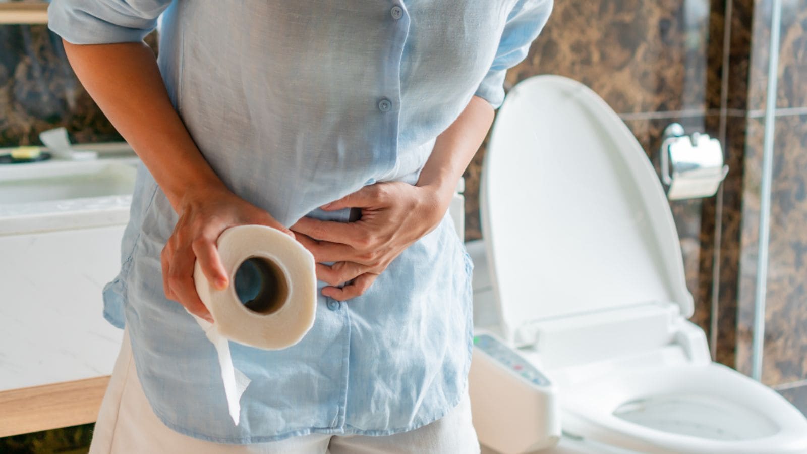 Young Asian woman's hand holding toilet paper and suffering from constipation, diarrhea, stomachache or cramps.