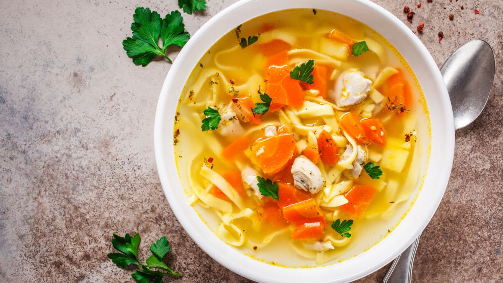 Chicken noodle soup with parsley and vegetables in a white plate