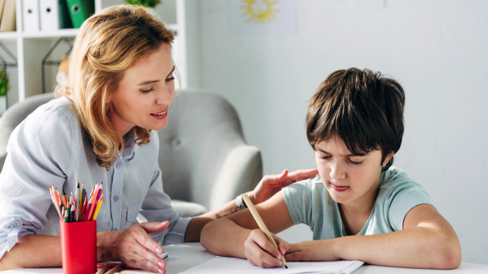 Kid with dyslexia drawing with pencil and child psychologist looking at it